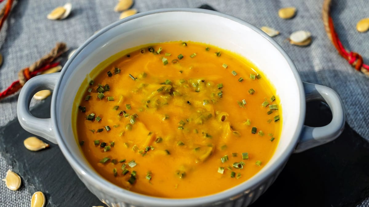 Velouté de légumes orange servi dans une cocotte, parsemé de ciboulette