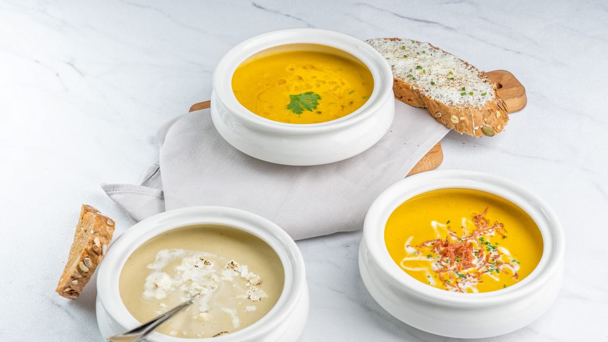 Trois bols de soupes maison, deux veloutés orange et une soupe crémeuse, avec du pain