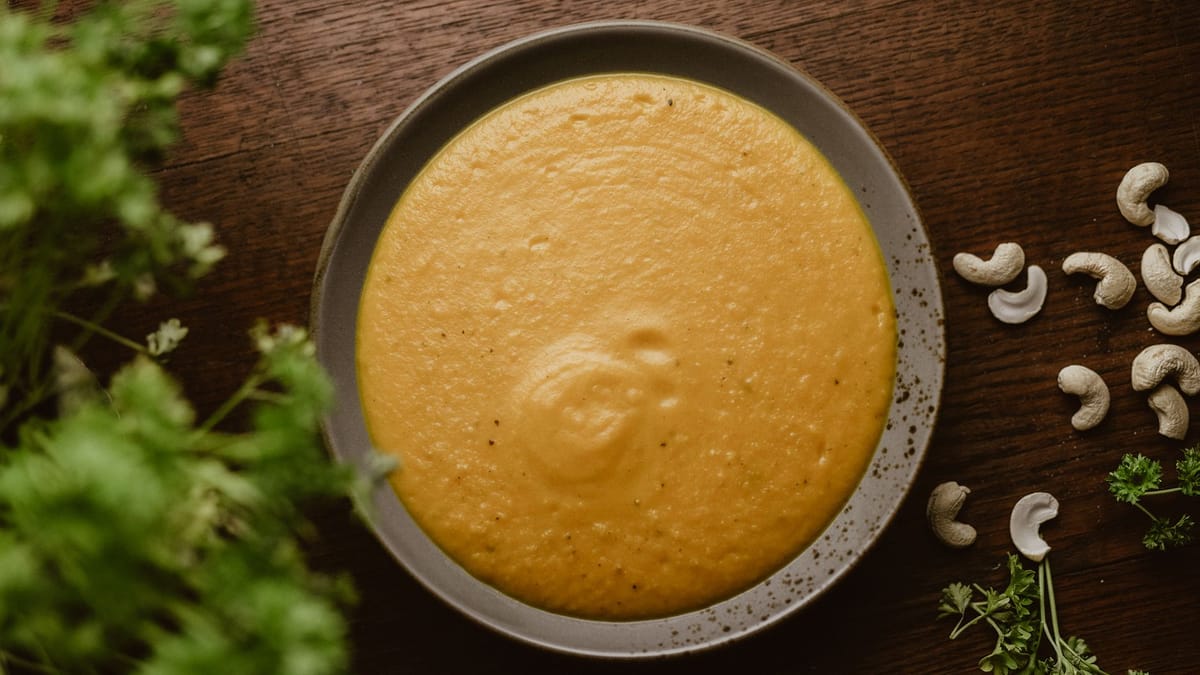 Assiette de velouté orange bien lisse, entourée de noix de cajou et d'herbes